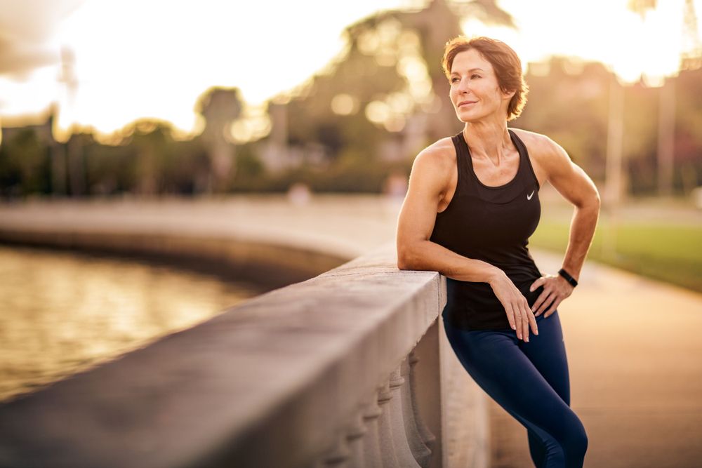 Athlete resting on railing during sunset workout by waterfront.