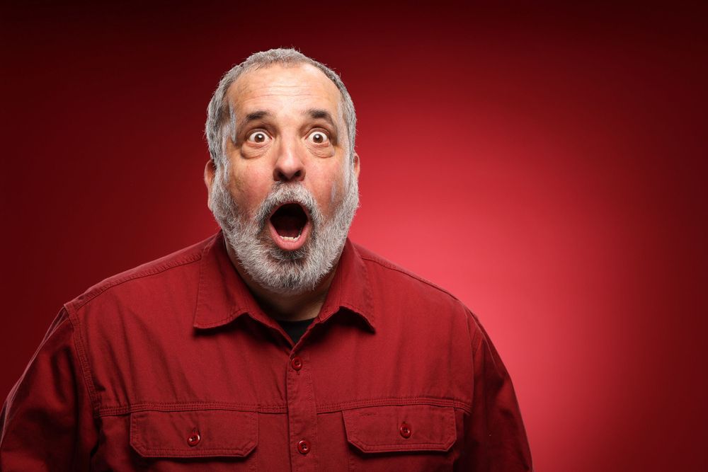 Person wearing red shirt making exaggerated surprised expression against red background.