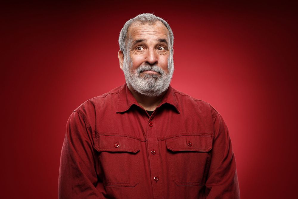 Portrait showing thoughtful expression against red backdrop wearing casual button-up shirt.