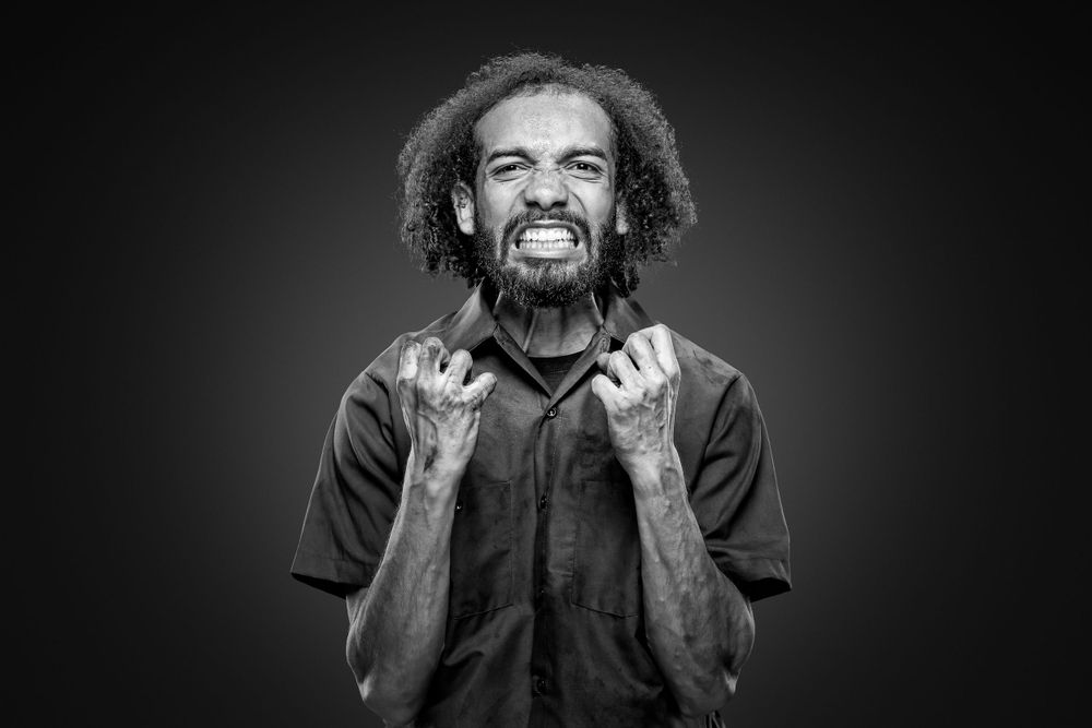 Expressive black and white portrait showing intense emotion with clenched fists against dark background.