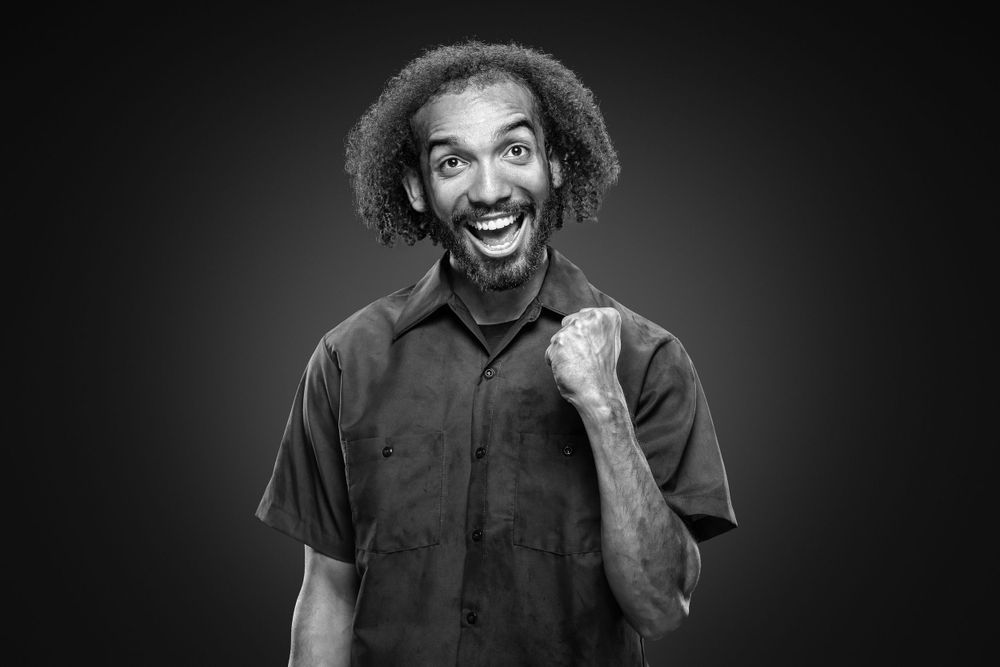Black and white portrait showing joyful expression with raised fist gesture.