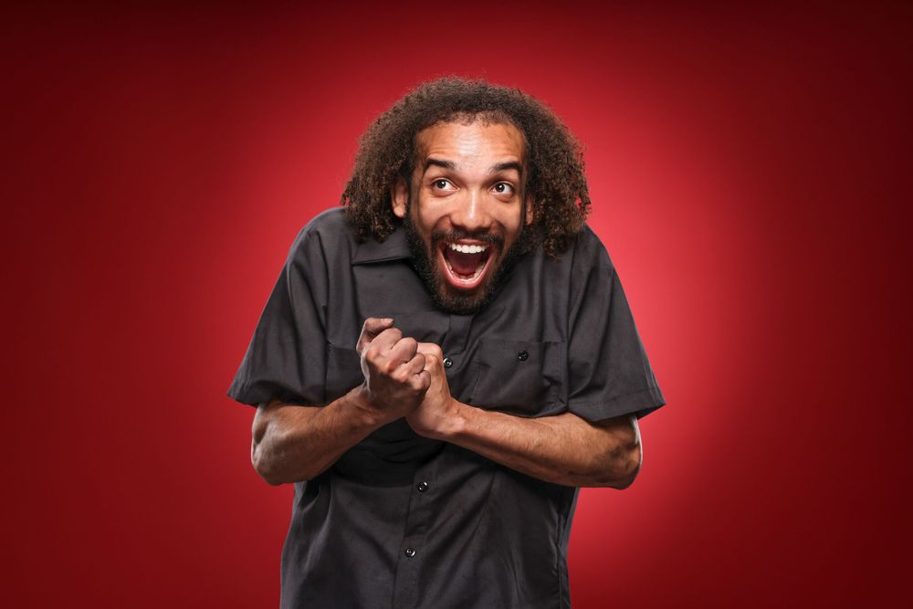 Person with curly hair and a black shirt showing excited expression against a red background.