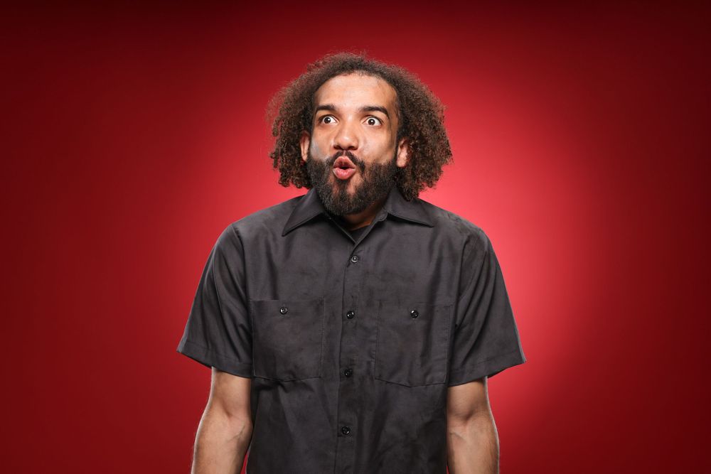 Playful portrait of someone making silly crossed eyes and sticking out their tongue against a red background.