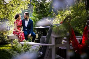 Un couple mixte asiatique et caucasien, en tenue de mariage traditionnelle, est assis en plein air, entouré d'une végétation luxuriante.