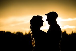 Des silhouettes de deux amoureux se détachent sur un ciel de coucher de soleil orangé spectaculaire, avec des arbres sombres à l'horizon.