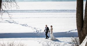 Un paysage hivernal enneigé avec un couple en habit de mariage se promenant le long d'une rive gelée par une belle journée ensoleillée.