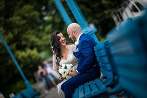Un couple de jeunes mariés du Moyen-Orient partage un moment romantique sur un banc bleu lors d'une séance photo de mariage en extérieur.