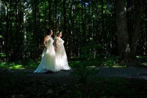 Deux femmes lesbiennes nouvellement mariées sont éclairées par un rayon de soleil et marchent main dans la main dans une forêt sombre.