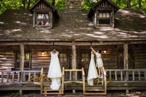 Deux robes de mariée blanches sont suspendues à l'extérieur d'une cabane rustique en rondins avec des lucarnes et un porche en bois.