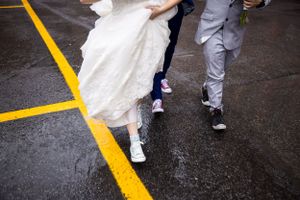Gros plan sur les pieds d’une mariée, son mari et un garçon d’honneur marchant le long d’une ligne jaune peinte sur un sol sombre.