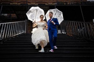 Une séance photo sous la pluie dans un escalier de L’Ambroisie et L’Espace Canal à Montréal, avec les mariés qui tiennent un parapluie.