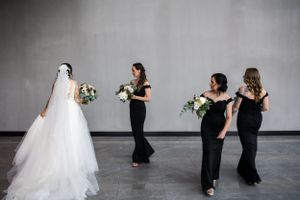 La mariée en robe blanche et ses demoiselles d'honneur en robes noires, tenant des bouquets, déambulent dans un espace moderne.