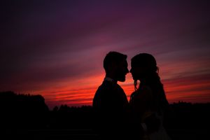 Silhouettes d’un couple amoureux se détachant sur un ciel de coucher de soleil aux teintes violettes et orangées éclatantes.