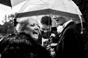 Moment capté sur le vif d’un groupe de personnes, parapluie à la main, qui se rassemble sous la pluie lors d'un mariage en plein air.
