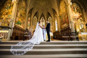Une cérémonie de mariage dans une cathédrale gothique aux plafonds voûtés spectaculaires. Le long voile de la mariée recouvre les escaliers.