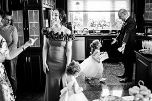 Moment capté sur le vif durant les préparatifs d’un mariage montrant des gens qui jasent et la bouquetière qui court vers son grand-père.