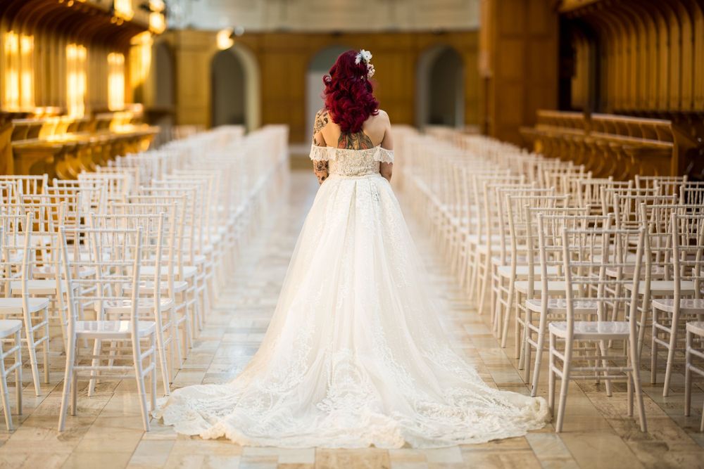 Portrait de la mariée de dos, avec son élégante robe de mariage blanche devant des rangées de chaises Chiavari, à l’Abbaye d’Oka.