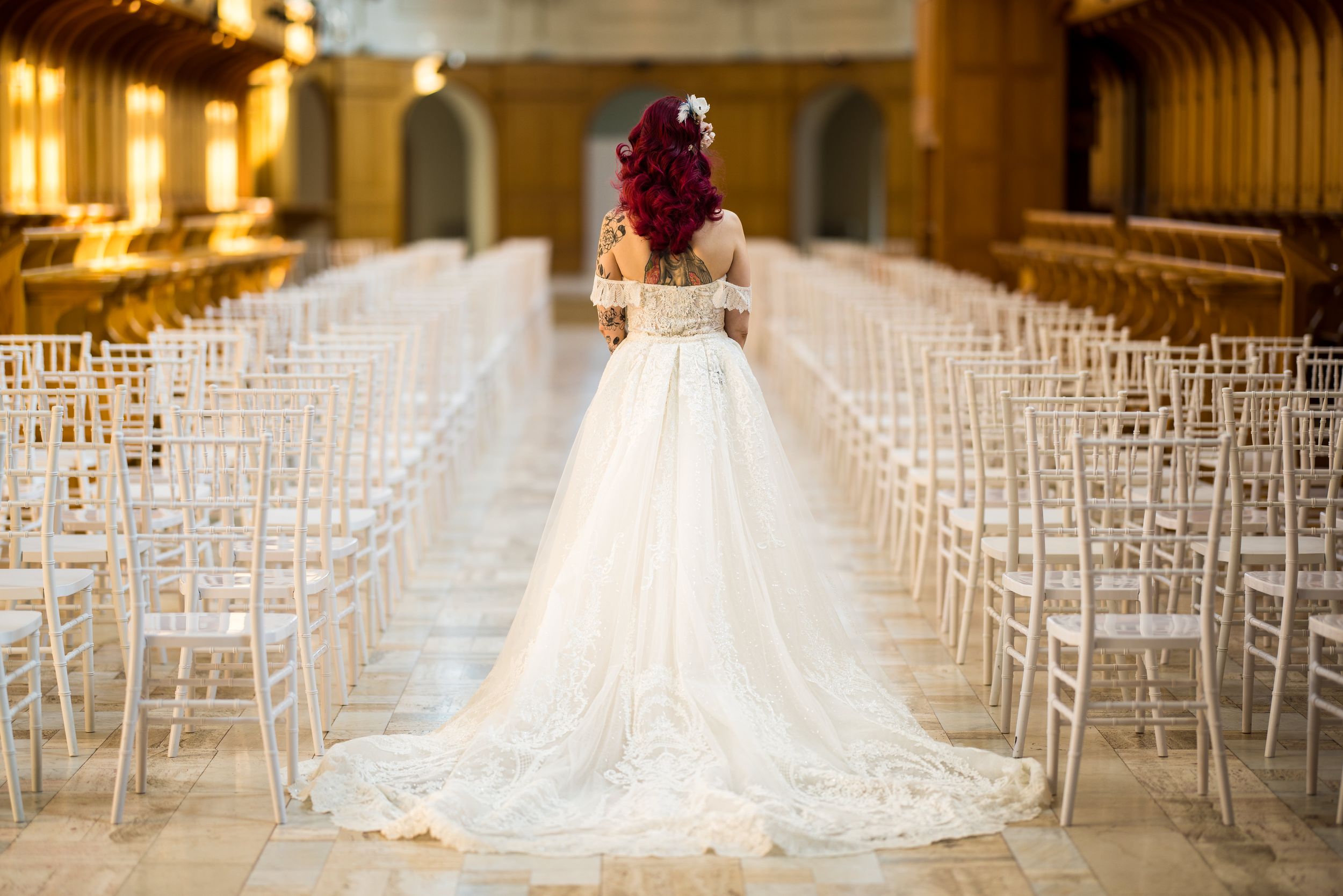 Portrait de la mariée de dos, avec son élégante robe de mariage blanche devant des rangées de chaises Chiavari, à l’Abbaye d’Oka.