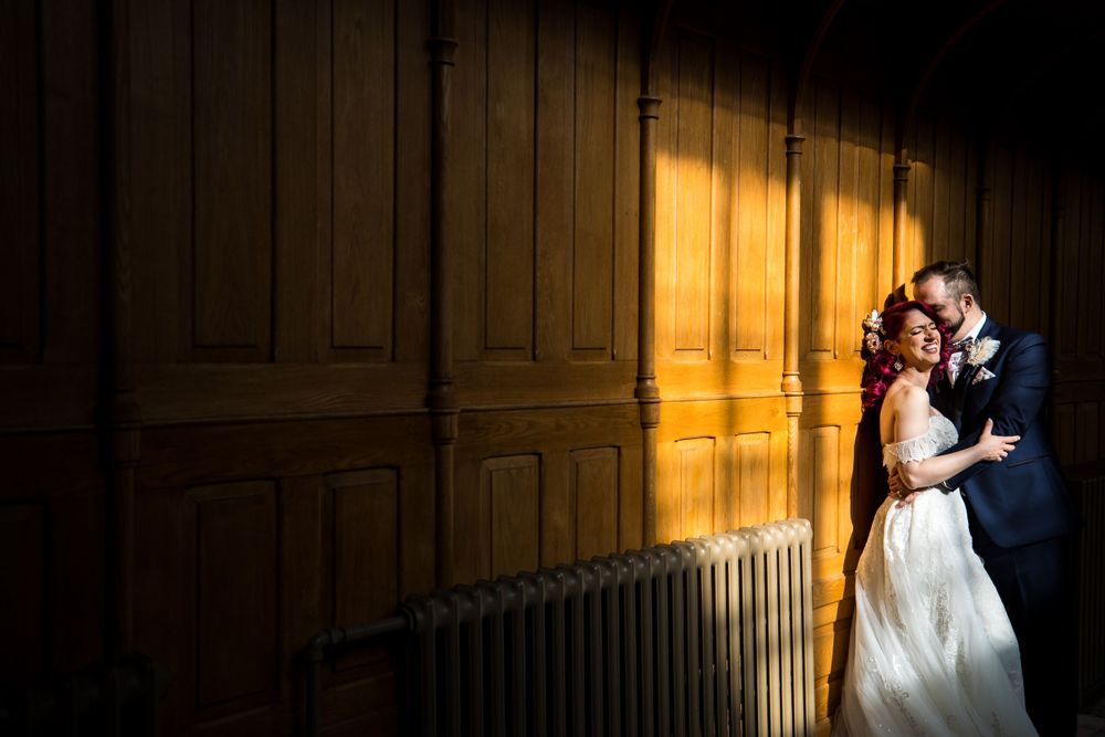 À l’Abbaye d’Oka, un couple partage un moment intime de mariage contre un mur en bois chaleureusement éclairé, avec des ombres dramatiques.