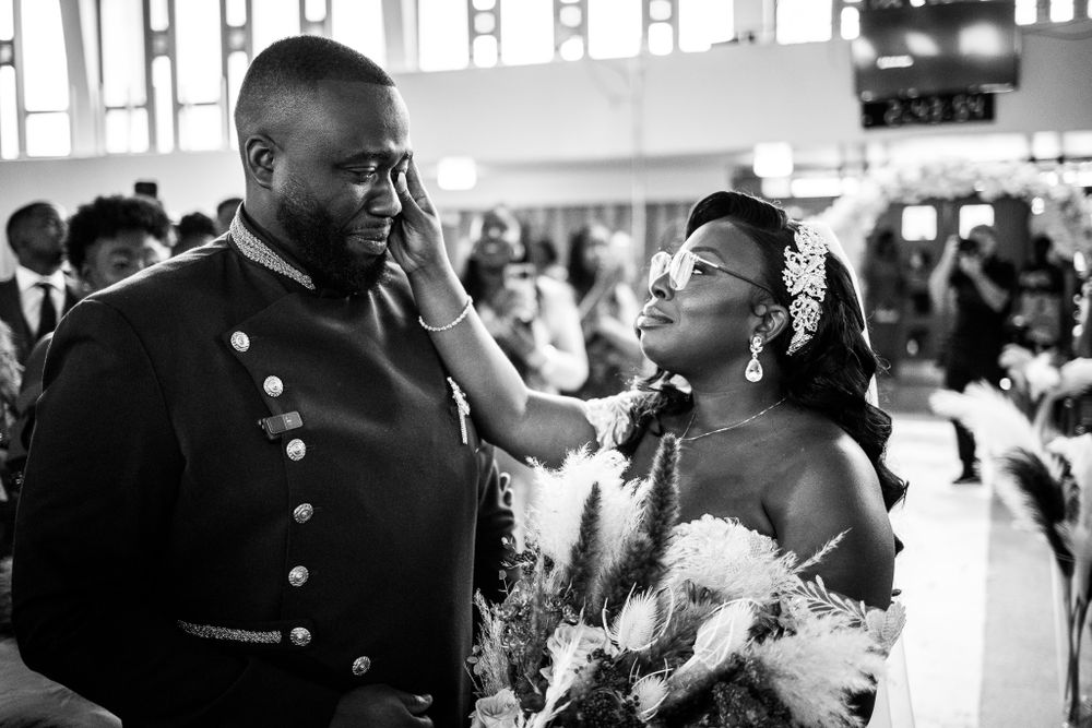 Photo en noir et blanc d’un moment touchant durant la cérémonie de mariage d’un couple à la peau noire, à l’église.