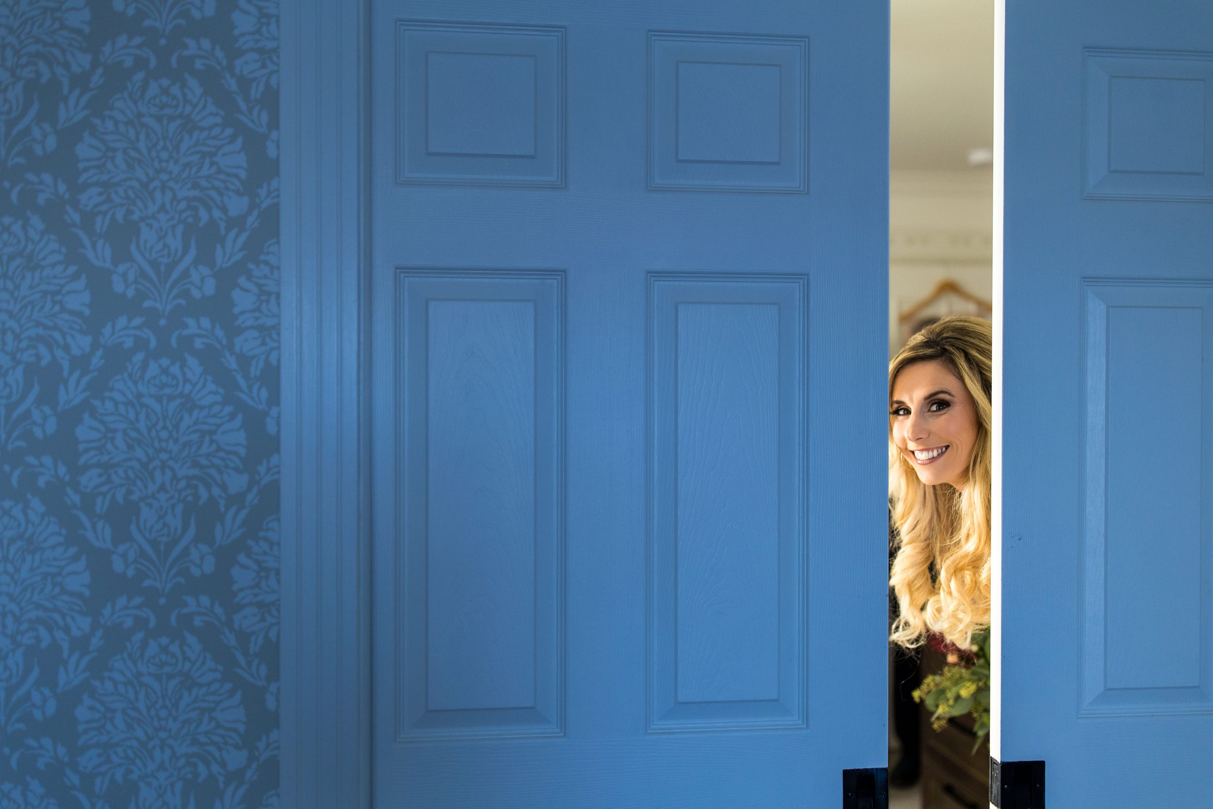 Deux portes bleutées sont entrouvertes et révèlent une mariée qui regarde en souriant, baignée d'un éclairage dramatique.