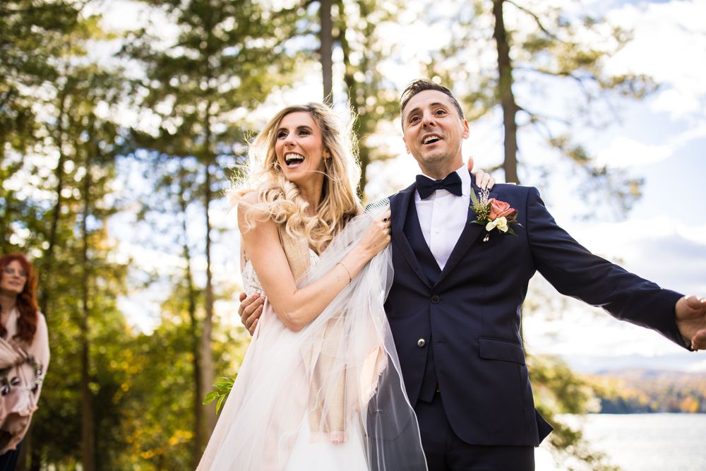 Un couple de mariés rayonnant de bonheur, rit ensemble en plein air, au milieu de grands pins, en ce jour de mariage à l’auberge Ripplecove.
