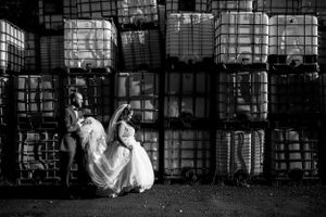 Un marié tient la robe de sa femme tandis qu'ils marchent devant des conteneurs industriels au Château Taillefer Lafon.