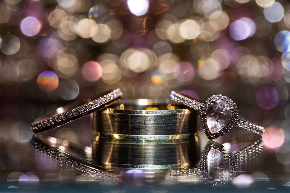 Trois élégantes alliances de mariage présentées ensemble, avec des lumières scintillantes floues en arrière-plan.