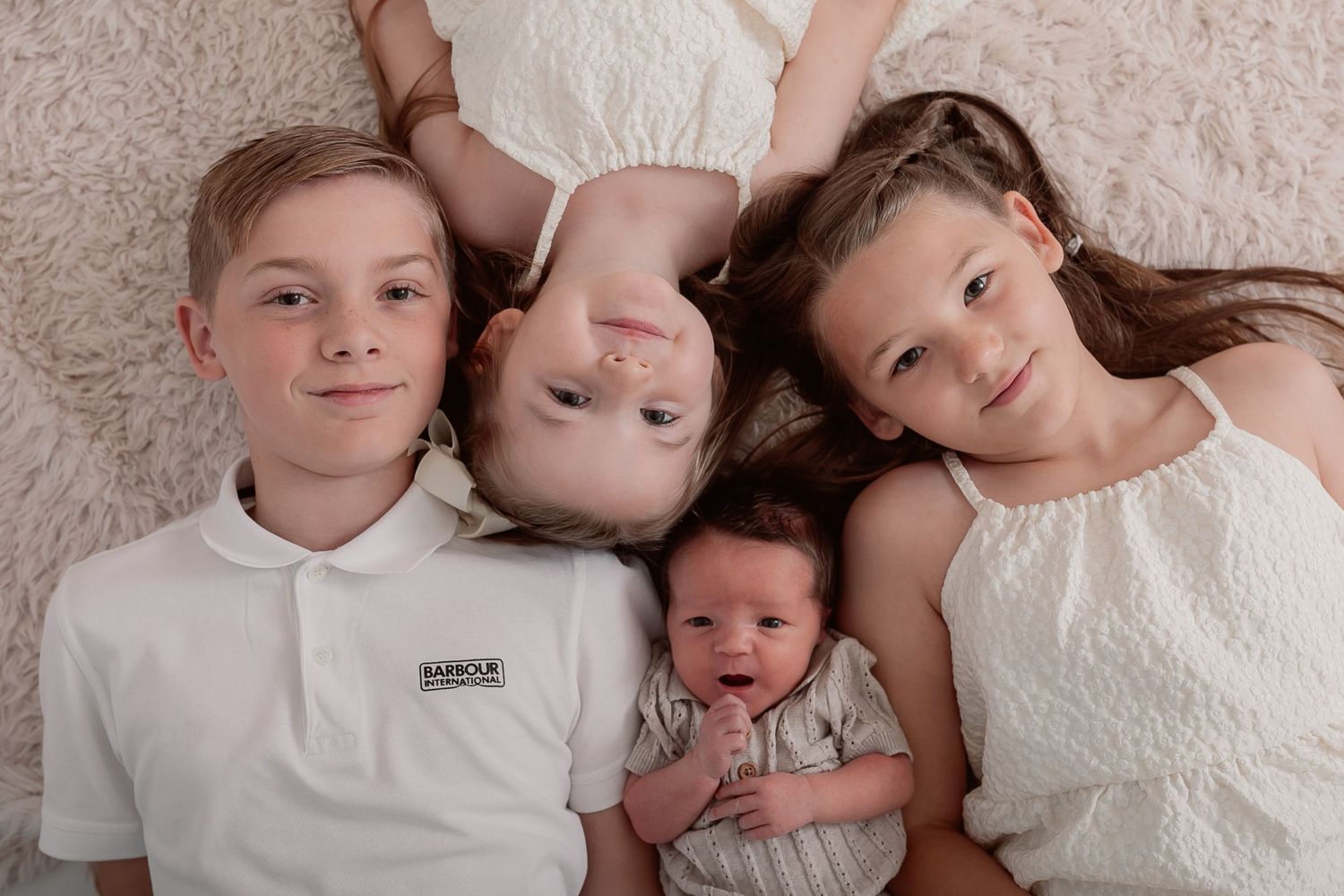 Siblings in white outfits laying together on light grey background. Photographer. Hull. East Yorkshire. Photography