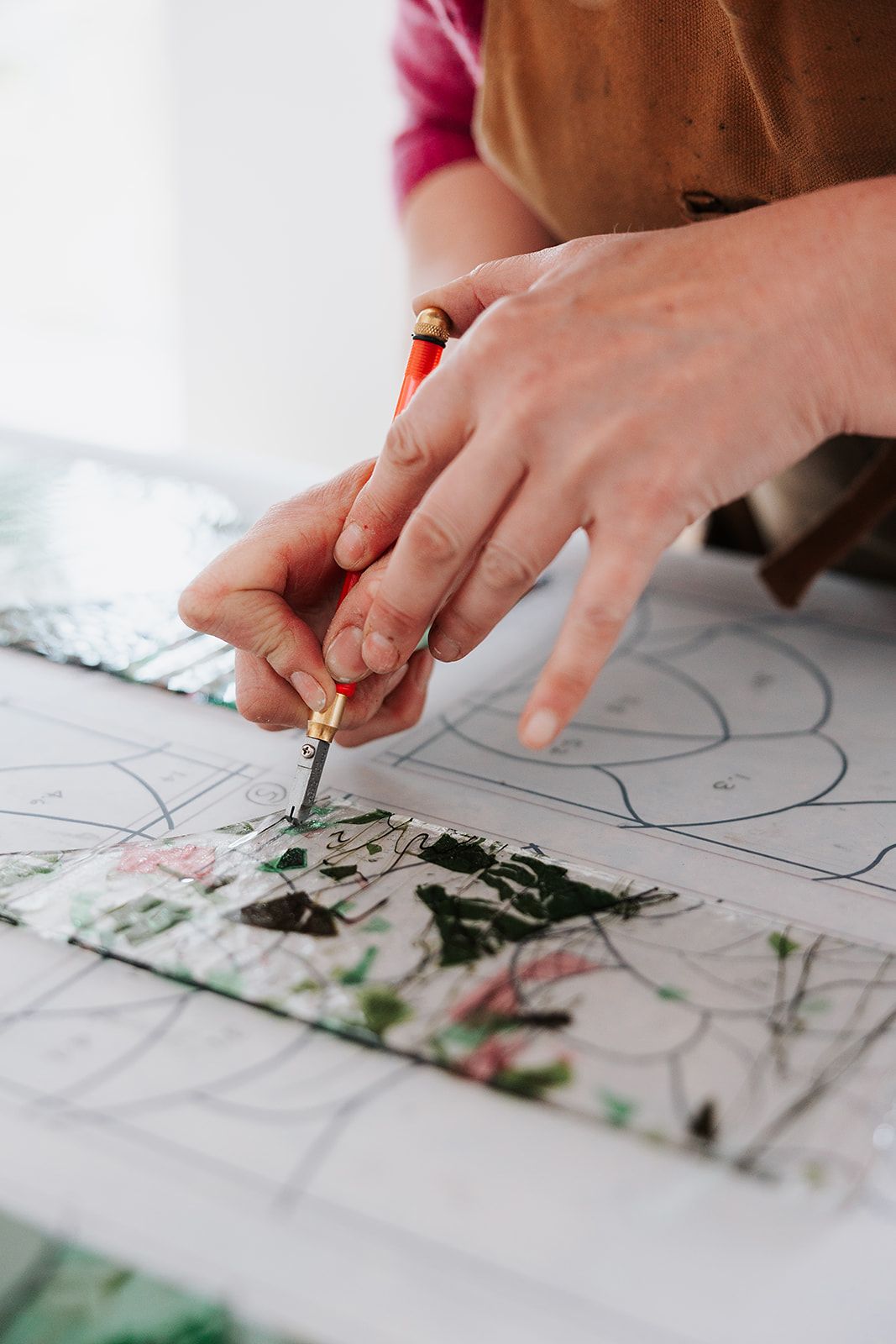 Close-up view of hands holding a pencil while drawing or coloring on paper with green and black artwork visible.