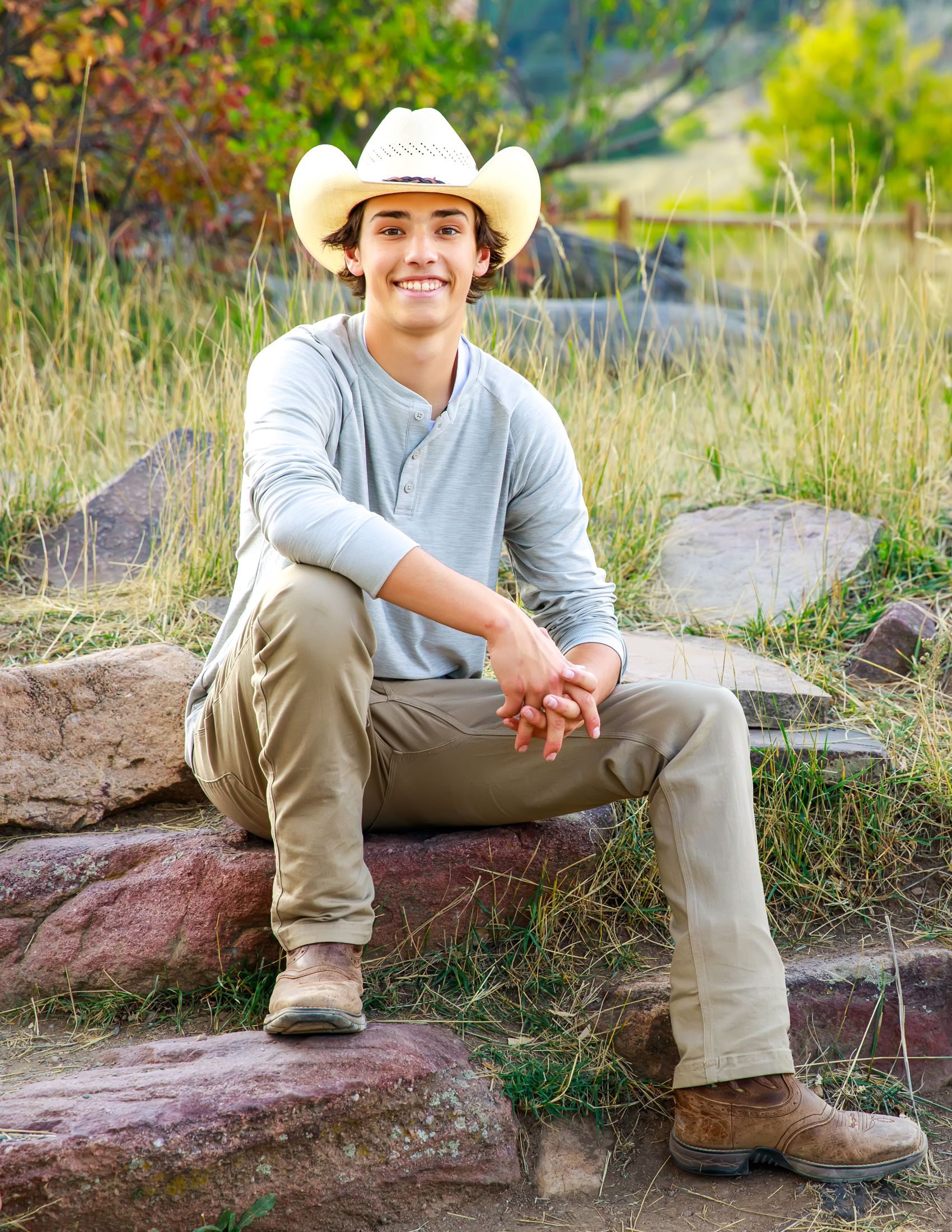Someone wearing a cowboy hat and casual clothing sits casually on red rocks in an outdoor setting.