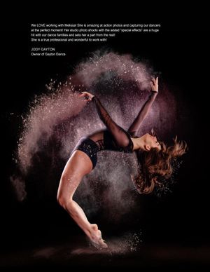 Dancer performs in dramatic black backdrop with white powder creating ethereal effect during movement sequence.