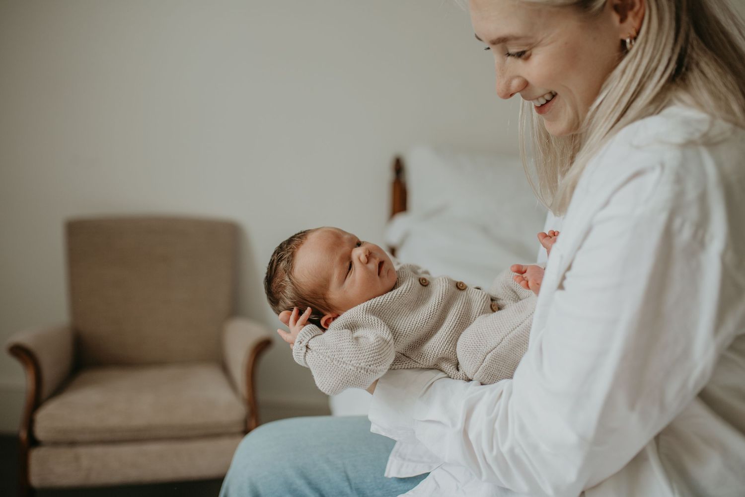 A tender moment captured between parent and baby in white clothing against a neutral background.