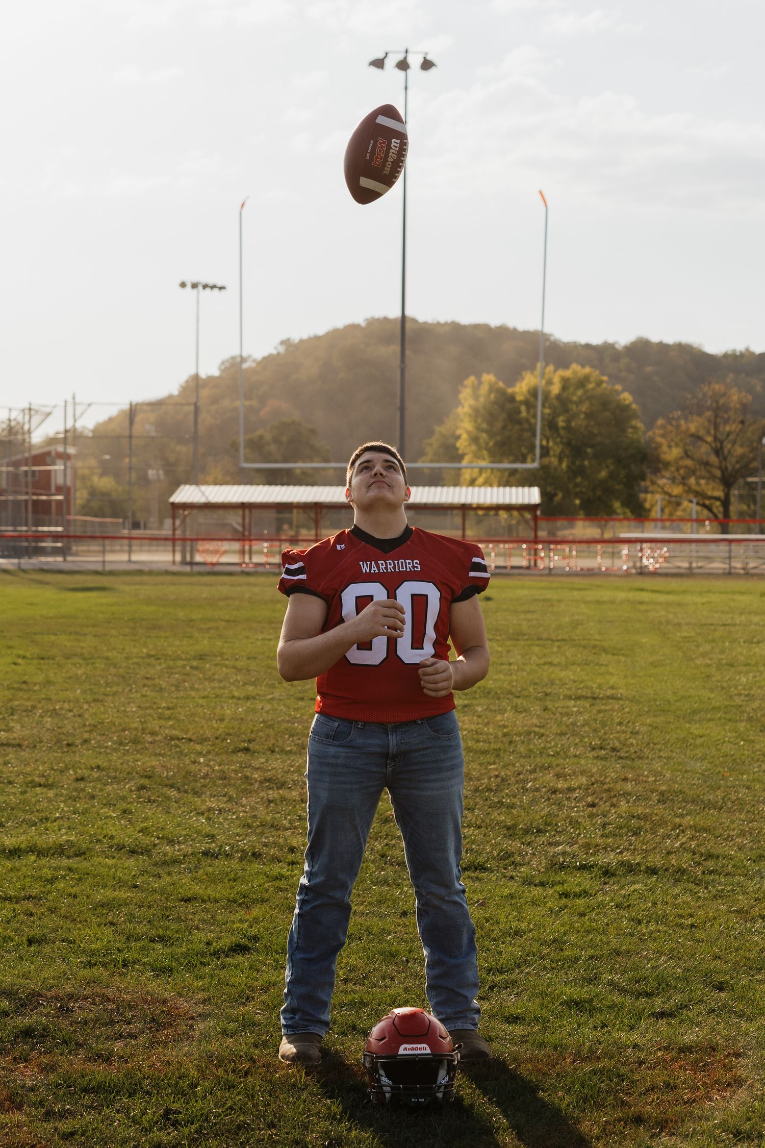 Football player poses with ball on grassy field during golden hour.