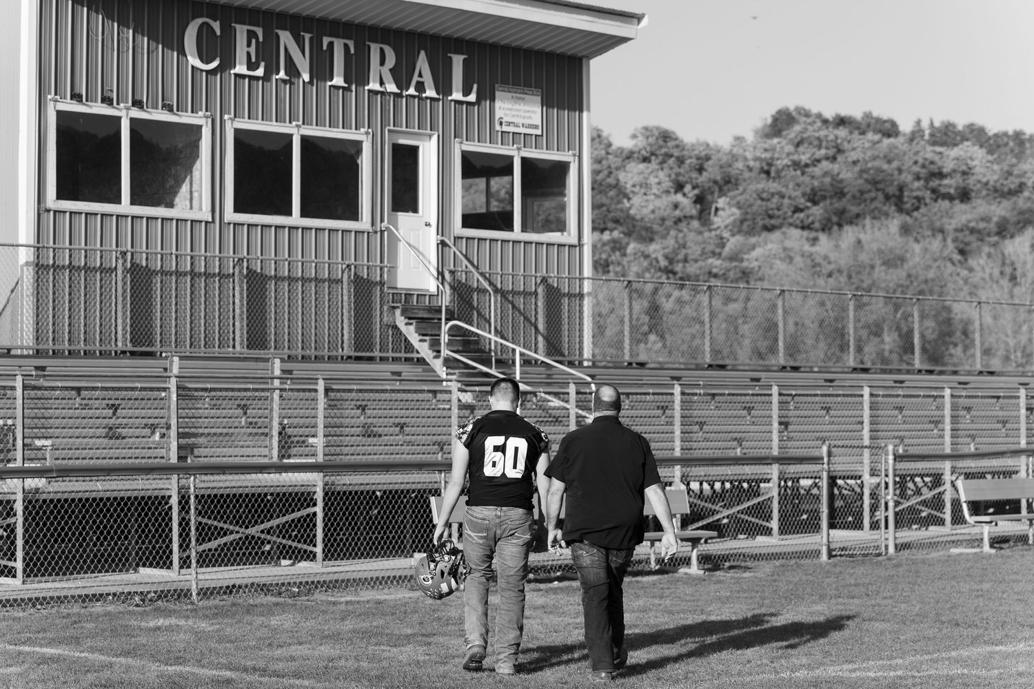 Vintage black and white panoramic view of a high school athletic field with bleachers and buildings in the background.