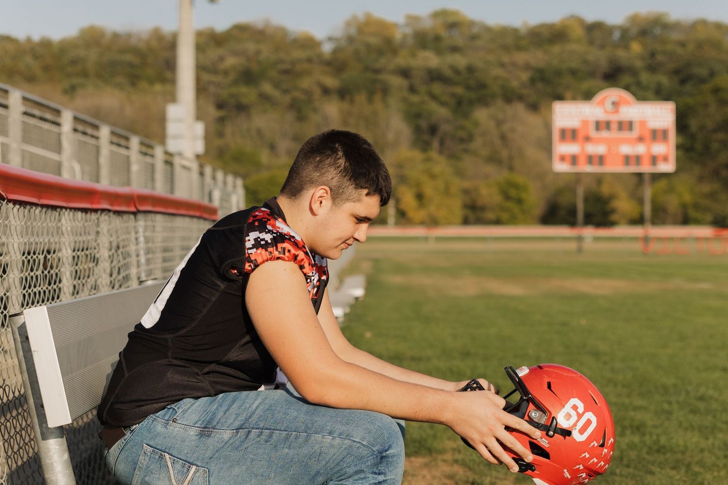 Football player in red jersey crouches low on field with stadium and scoreboard in background.