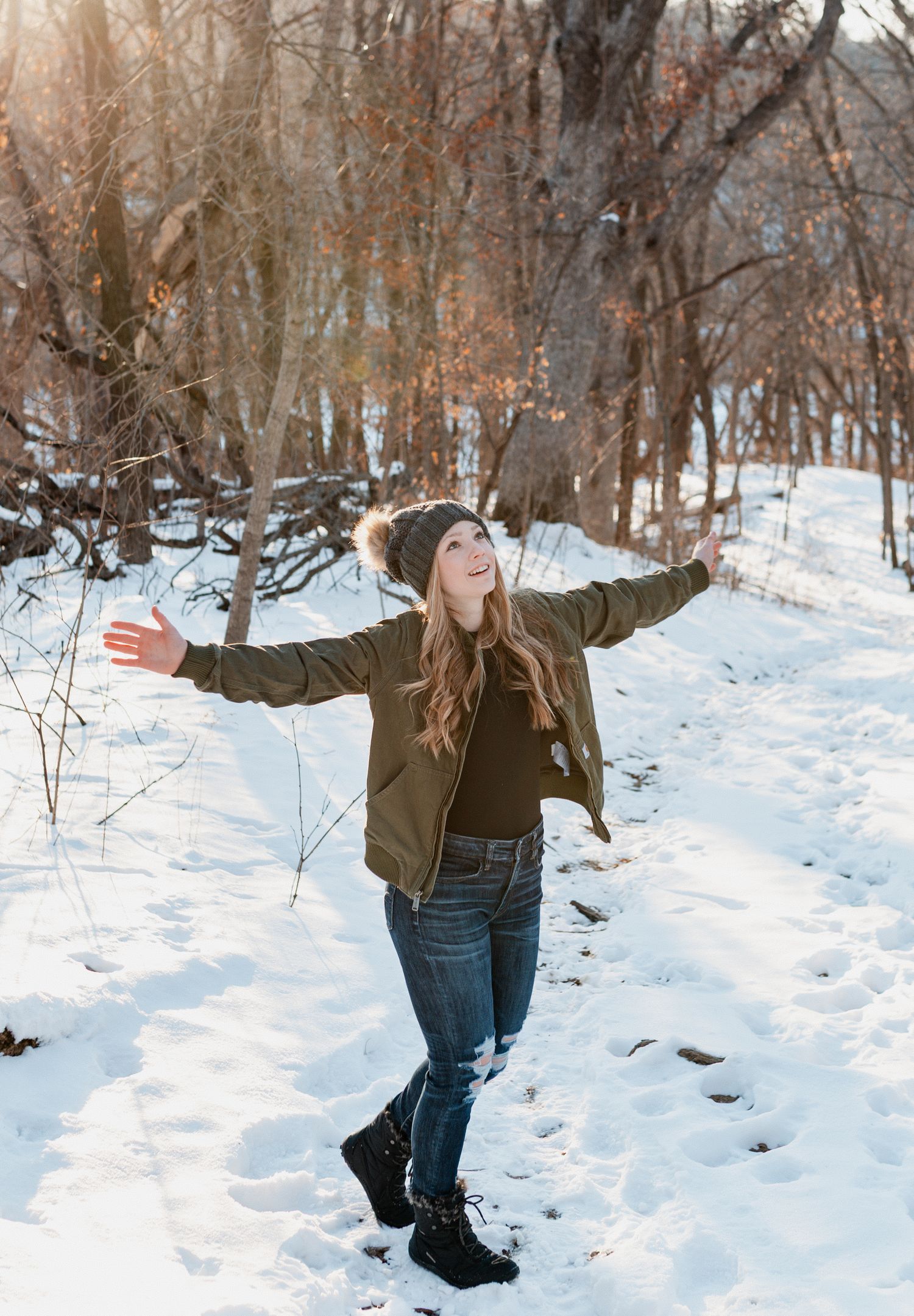 Person wearing winter clothing playfully throws snow in a snowy forest setting during a winter day.