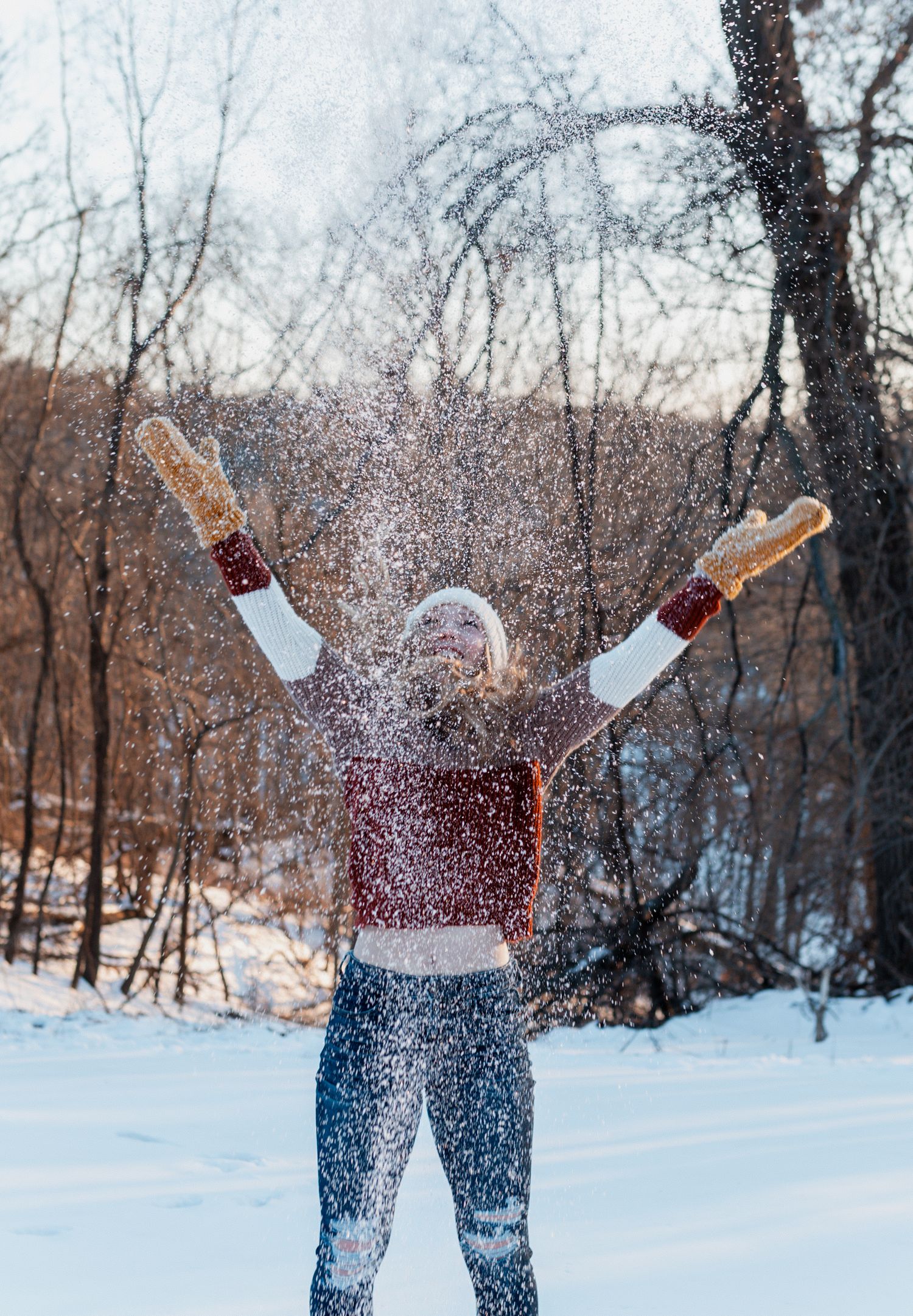 Person in winter clothing throws snow in the air creating a magical snowy effect in a forest landscape.