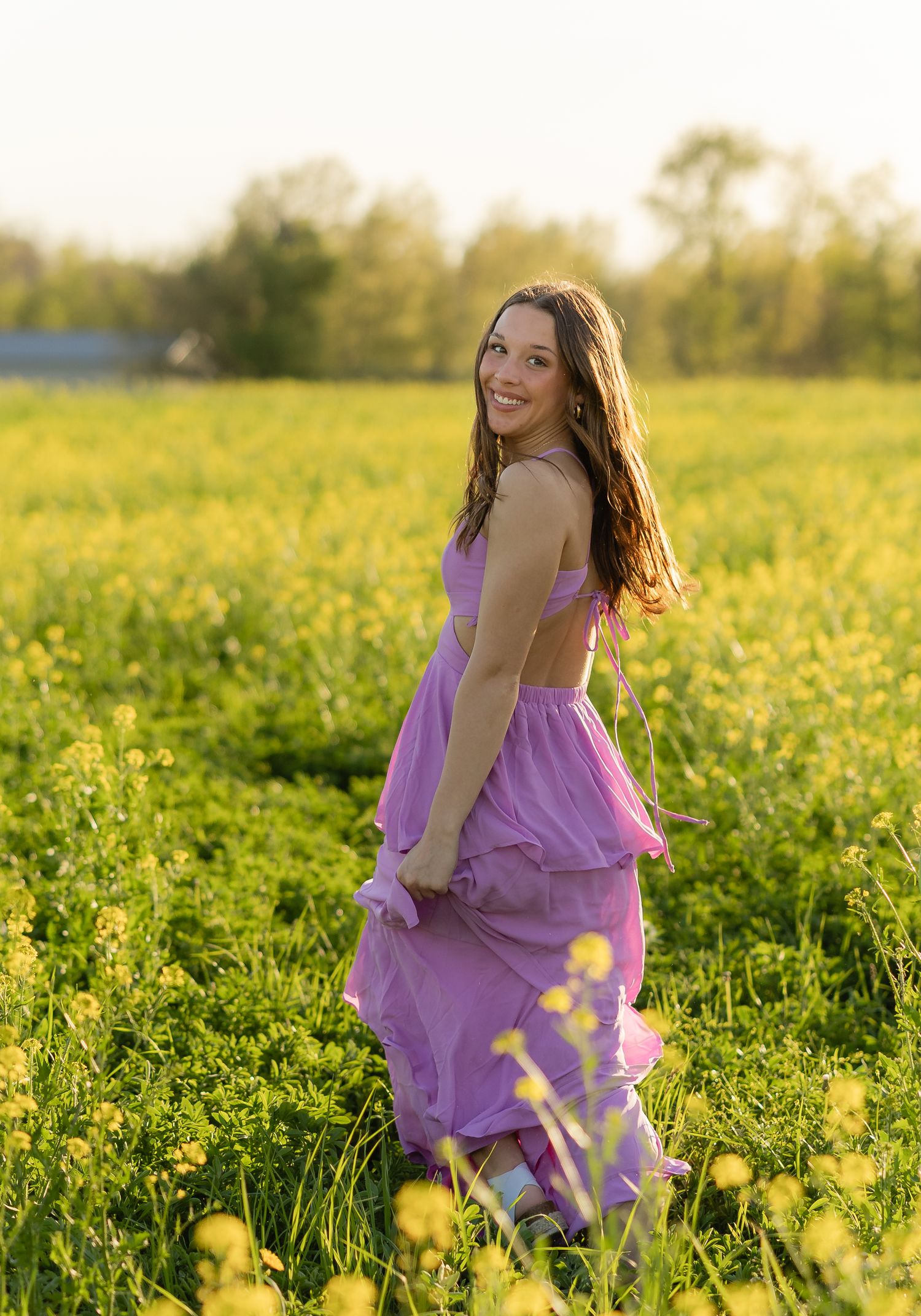 A person in a flowing lilac dress twirls gracefully in a sunlit meadow of yellow wildflowers during golden hour.