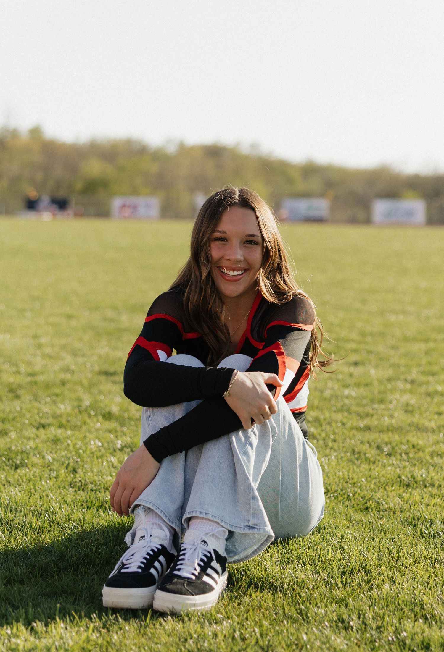 Student athlete sits on sunny grass field wearing sports uniform and white sneakers.