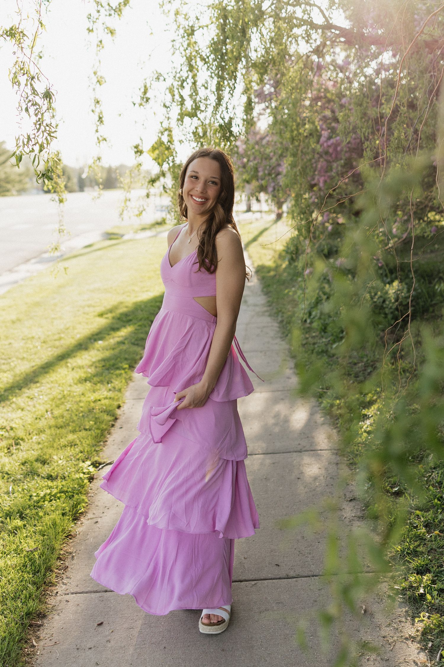 Person in ruffled purple sundress posing along garden path with sunlit foliage.