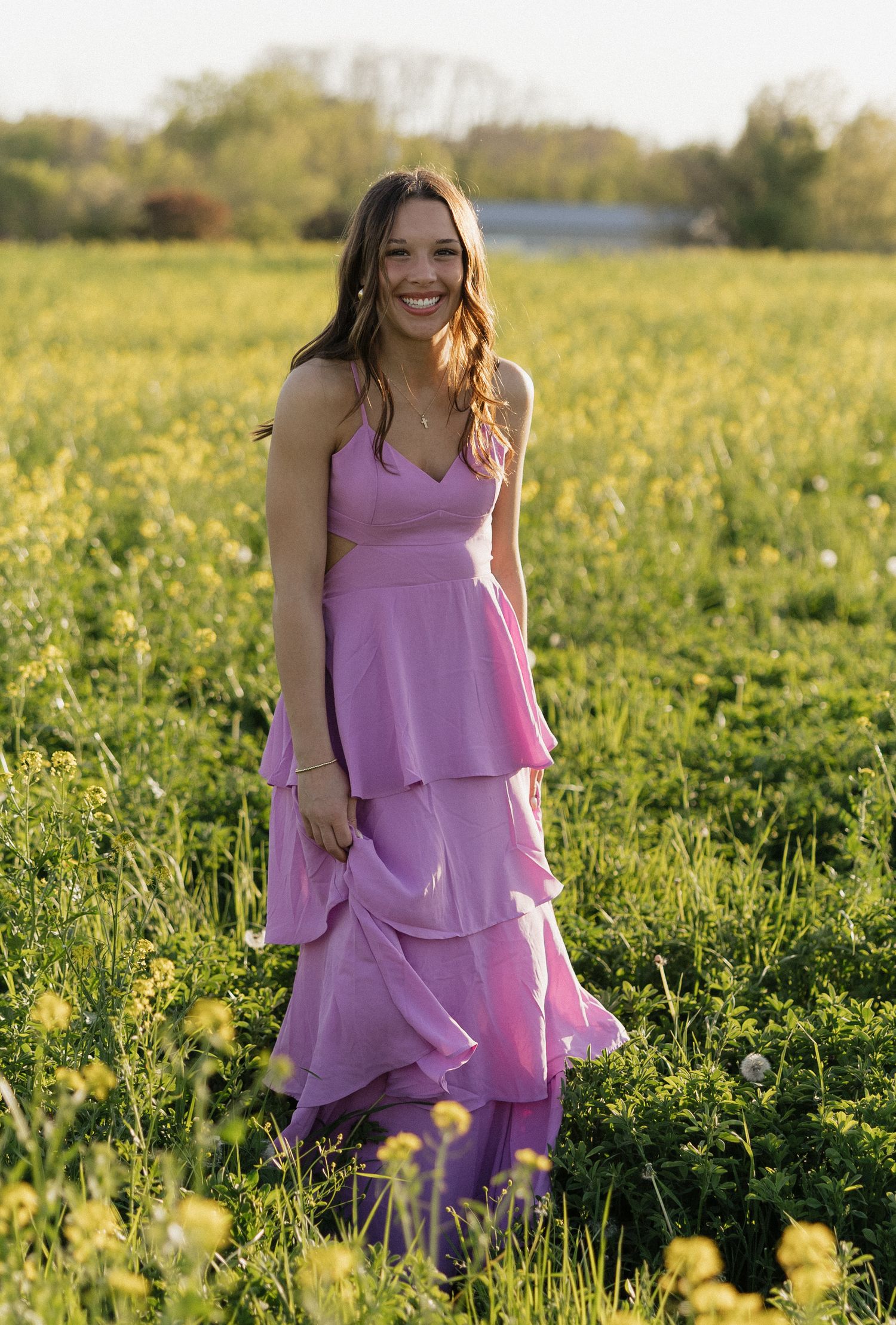 A person wearing a tiered lilac dress stands in a field of yellow wildflowers at golden hour.