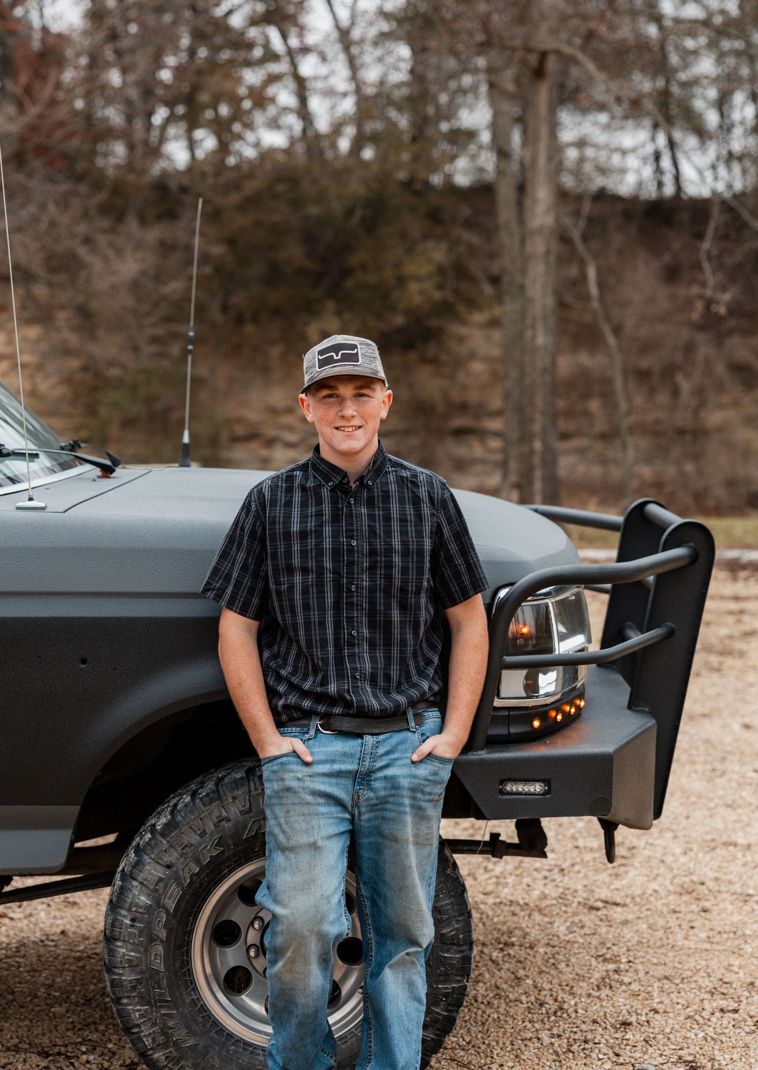 A lifted black pickup truck parked on gravel with a person leaning against it in a casual outdoor setting.