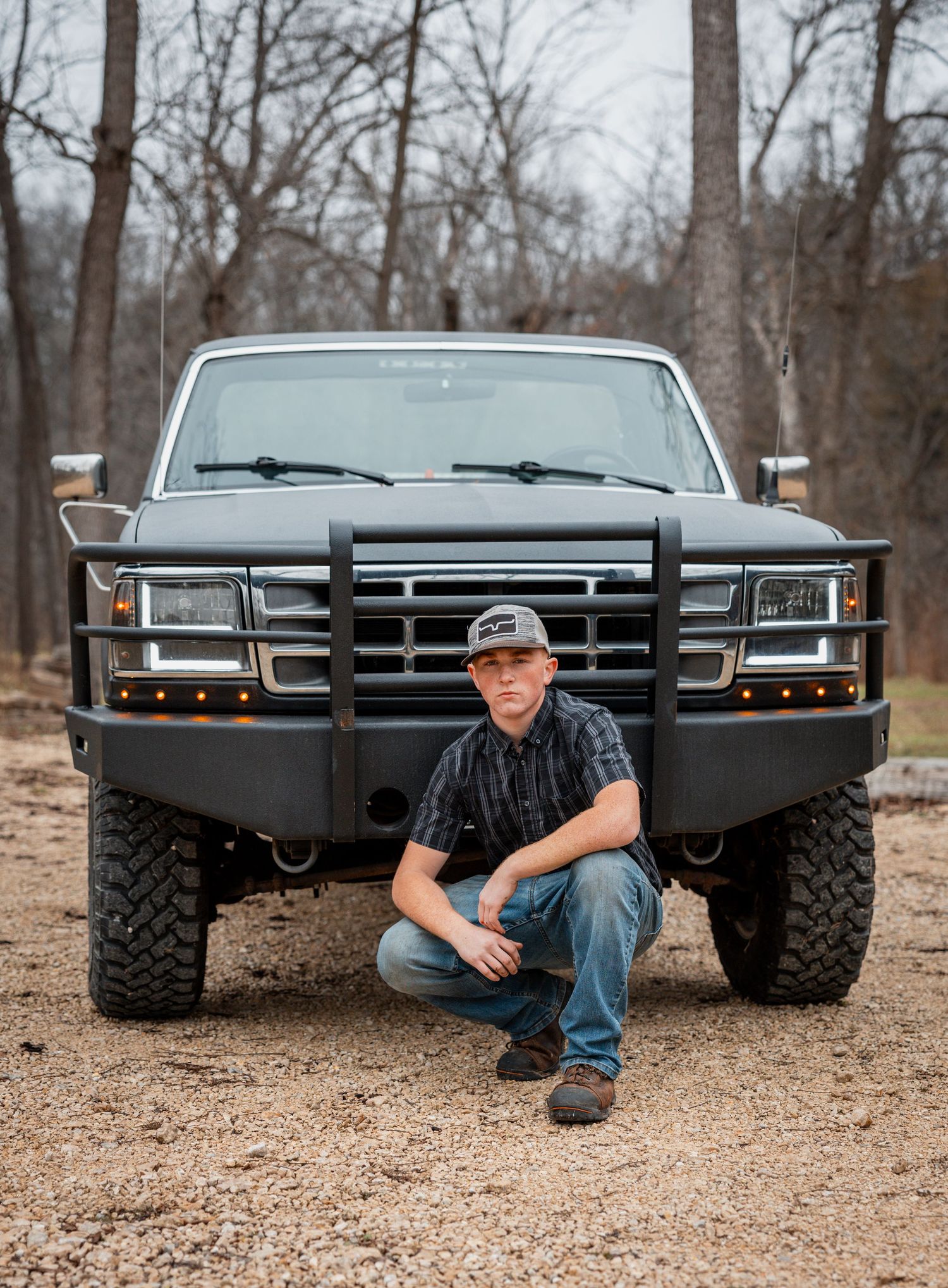 A black lifted truck with custom bumpers parked in a wooded area during autumn is shown from multiple angles.