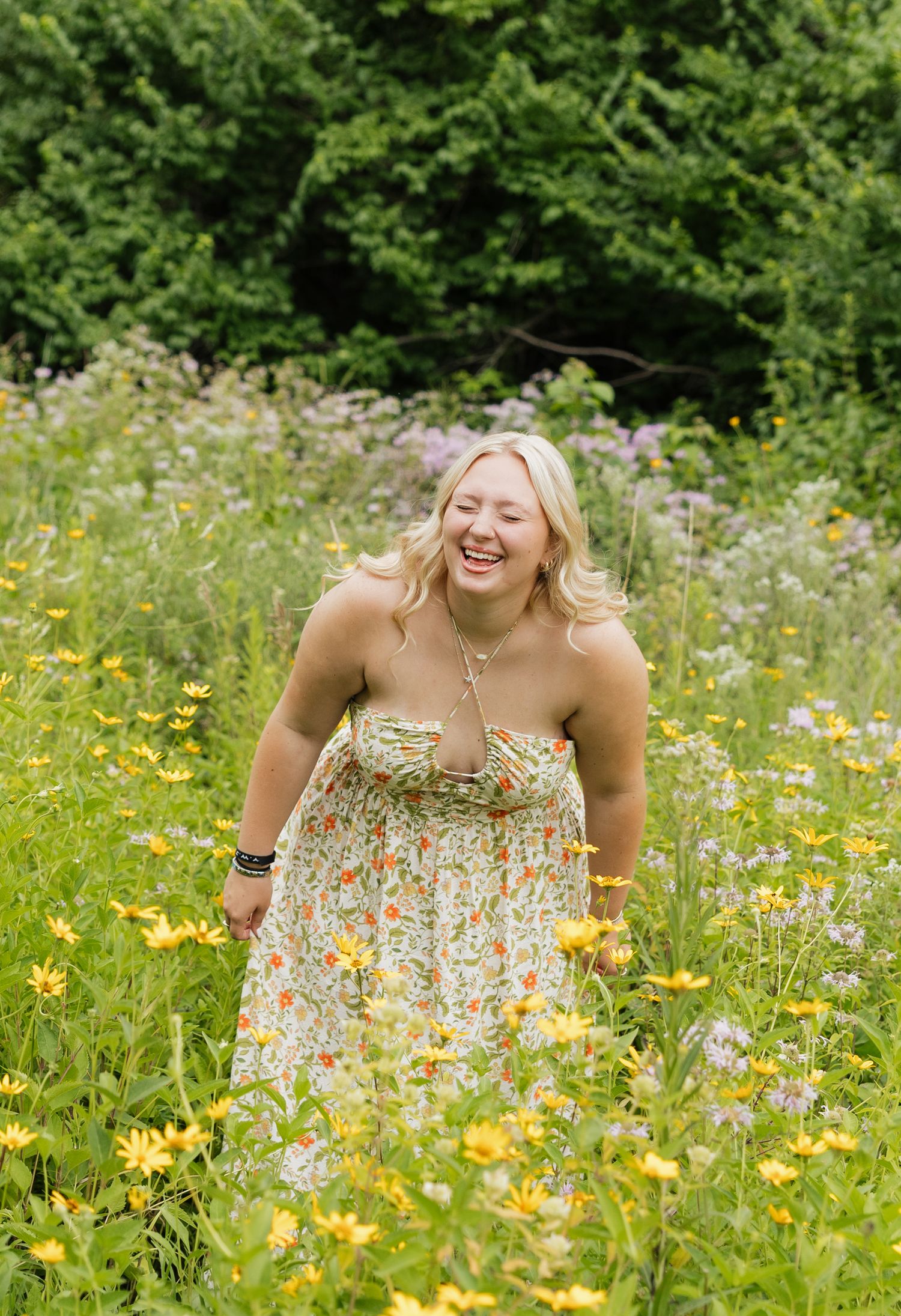 A person laughs joyfully while posing in a vibrant summer meadow filled with yellow and purple wildflowers.