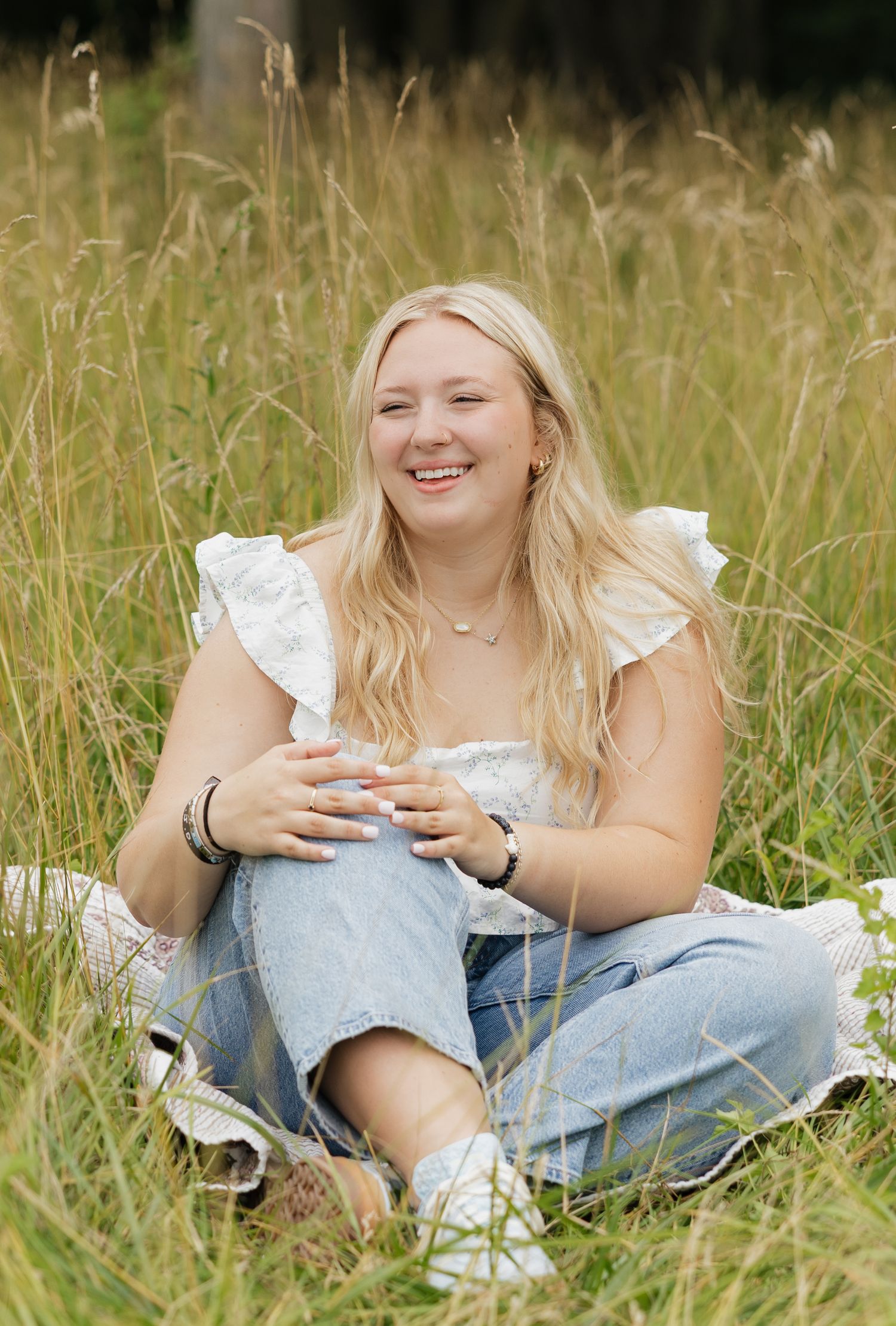 A person in a white top and jeans relaxes in a summer meadow with tall grass and natural lighting.