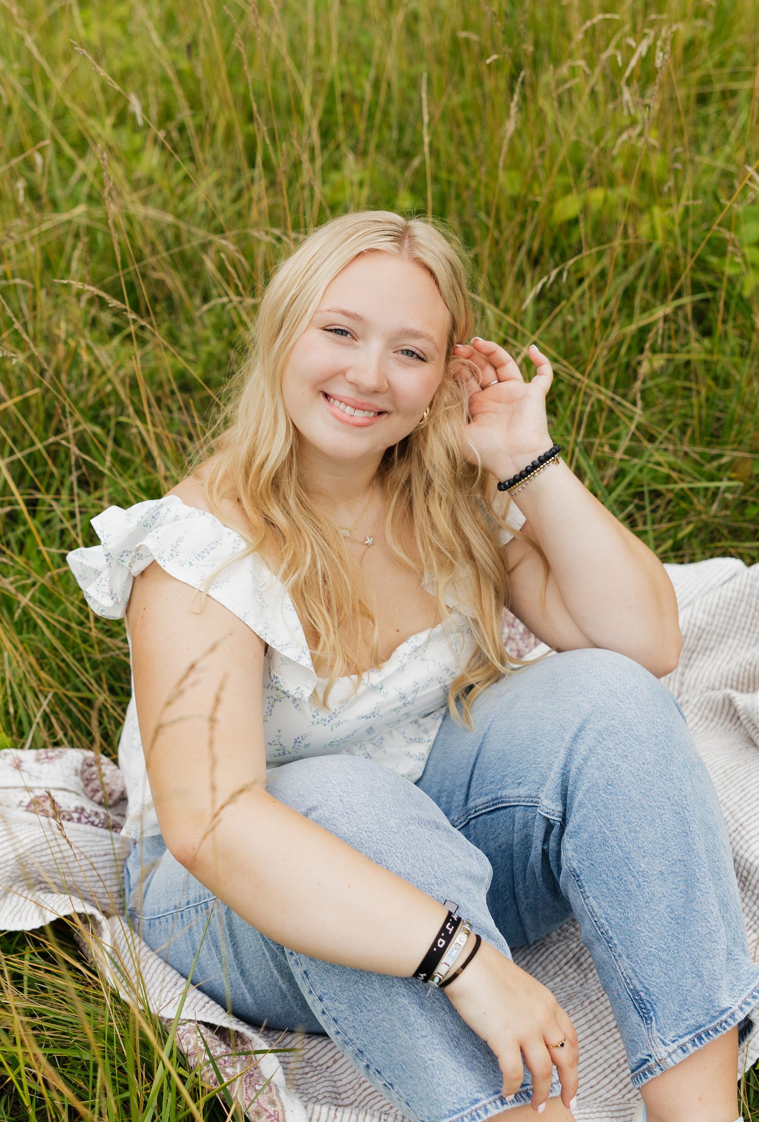 A person in a white top and jeans relaxes on a blanket in tall grass on a sunny day.
