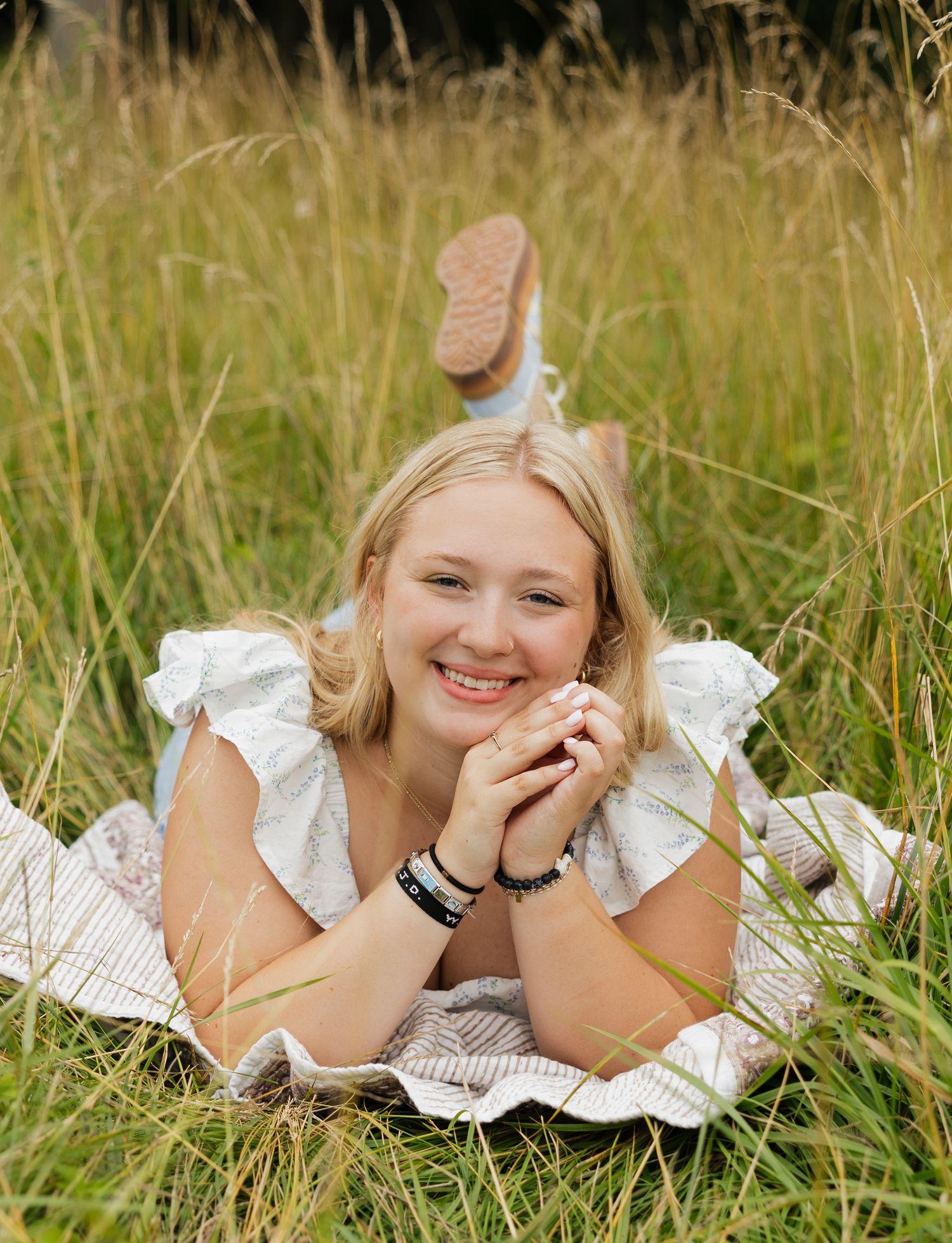 A person in a white dress lying in tall grass poses for a series of candid shots.
