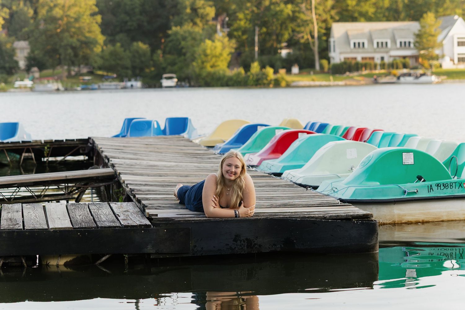 Colorful pedal boats and kayaks lined up along a wooden dock at a lake on a sunny autumn day.