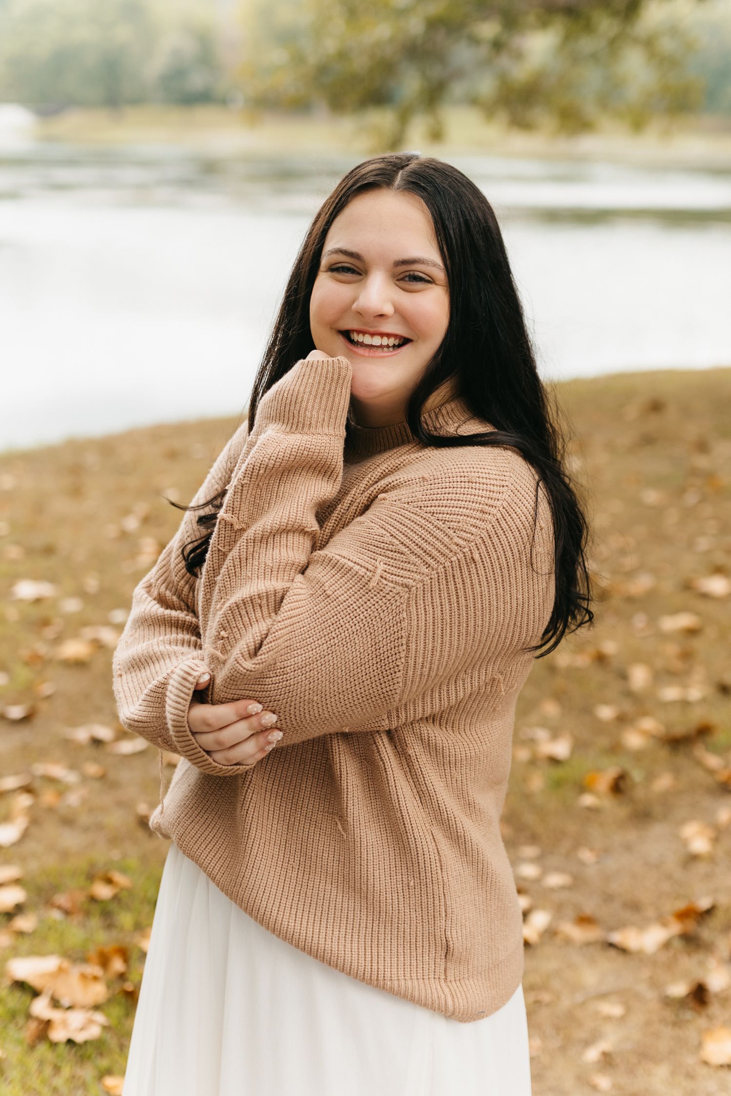 Series of joyful poses in a cozy beige sweater against a waterfront autumn backdrop with fallen leaves.